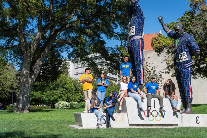 A diverse group of students sit around our Statue of John Carlos and Tommie Smith. 